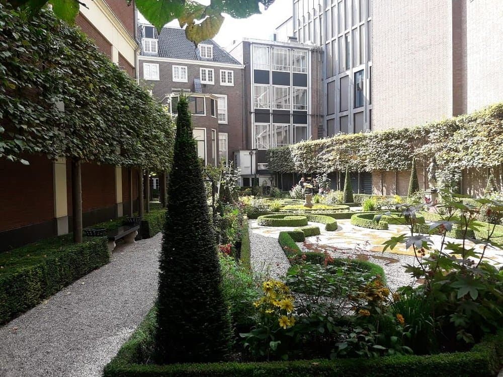 A lush, green courtyard (hofje) in Amsterdam Jordaan surrounded by historic red-brick houses