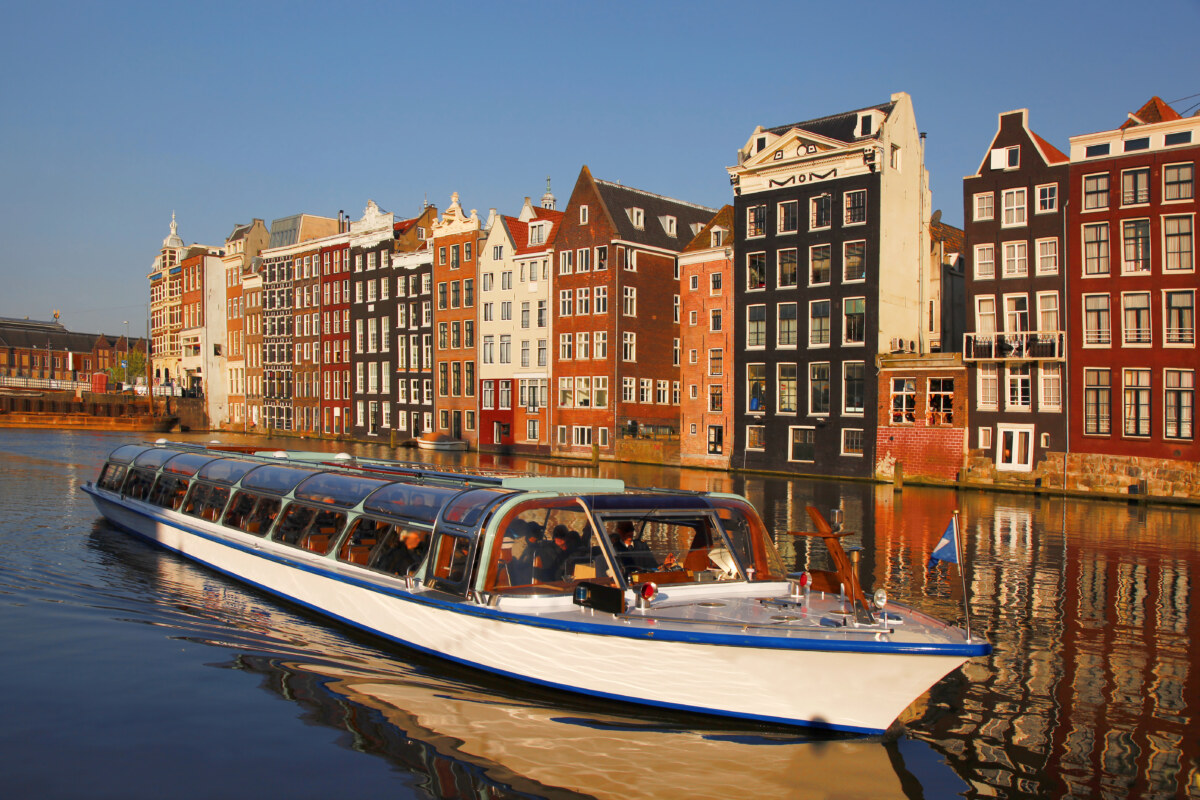 Amsterdam on a Budget: 10 Free and Low-Cost Activities for Travelers 1 Close-up of a motor boat cruising the canal and passing by the colorful houses in Amsterdam, Netherlands