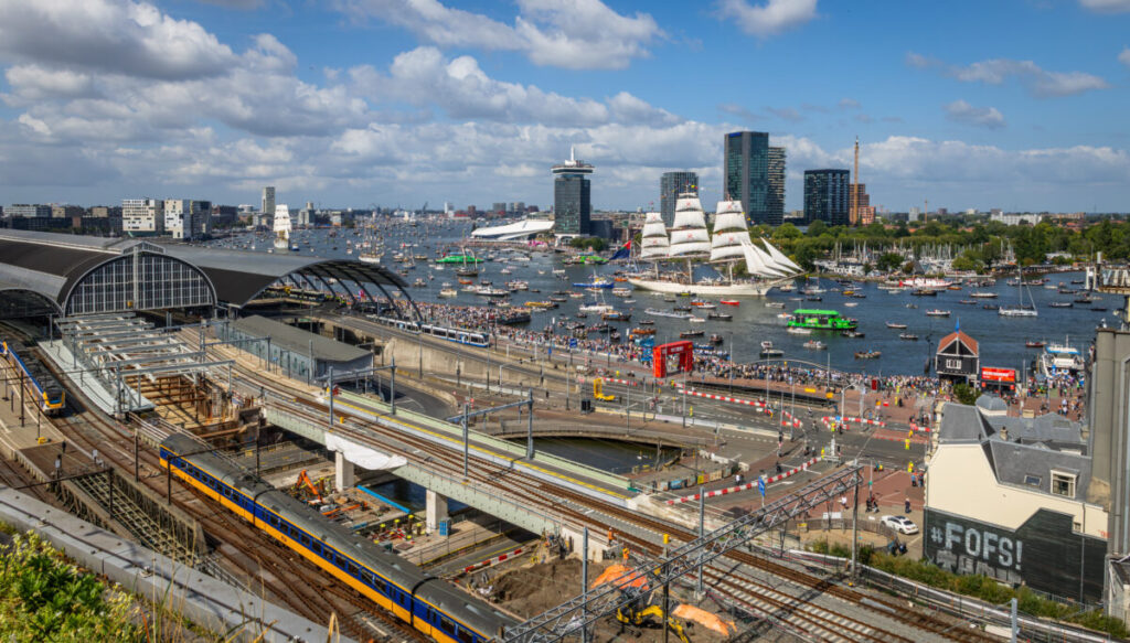 Amsterdam Airport Train vs Taxi: Which Is Better in 2026? 4 Tracks and yellow NS trains beside Amsterdam Centraal Station
