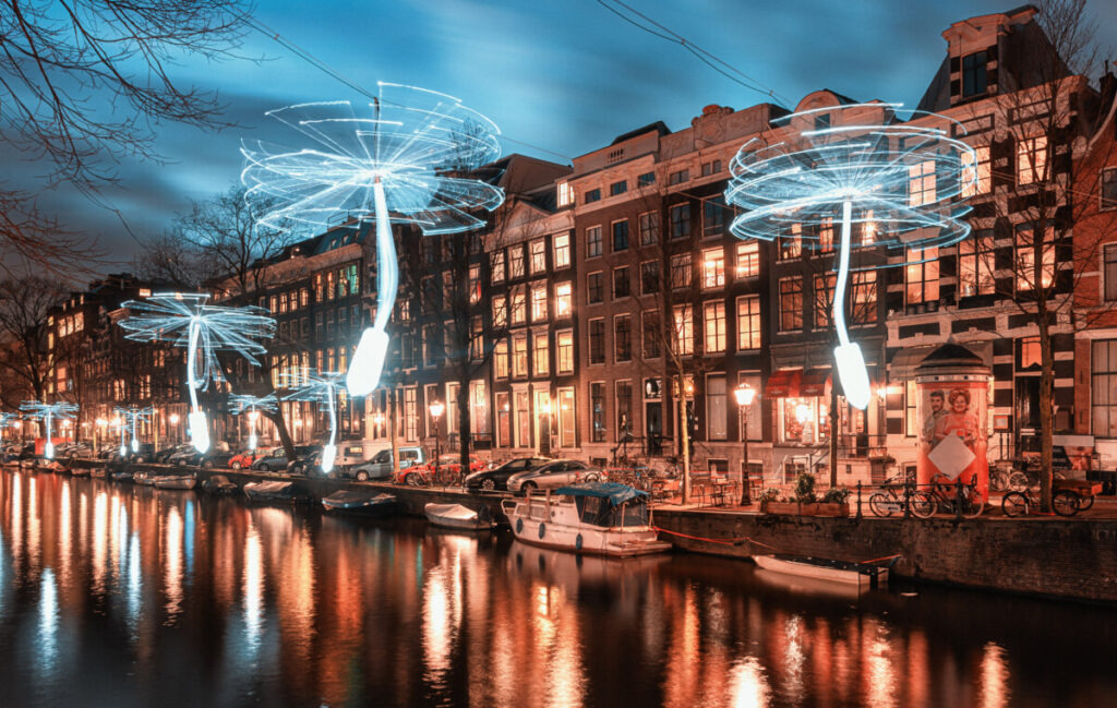 Wind-driven propellers illuminated in white light hover above the Herengracht in Amsterdam's old town during the Amsterdam Light Festival