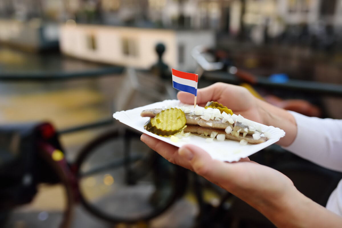 The Ultimate Guide to Amsterdam’s Best Street Food 1 Woman holding a plate of the Dutch herring street food with onion and cucumber in Amsterdam, Netherlands