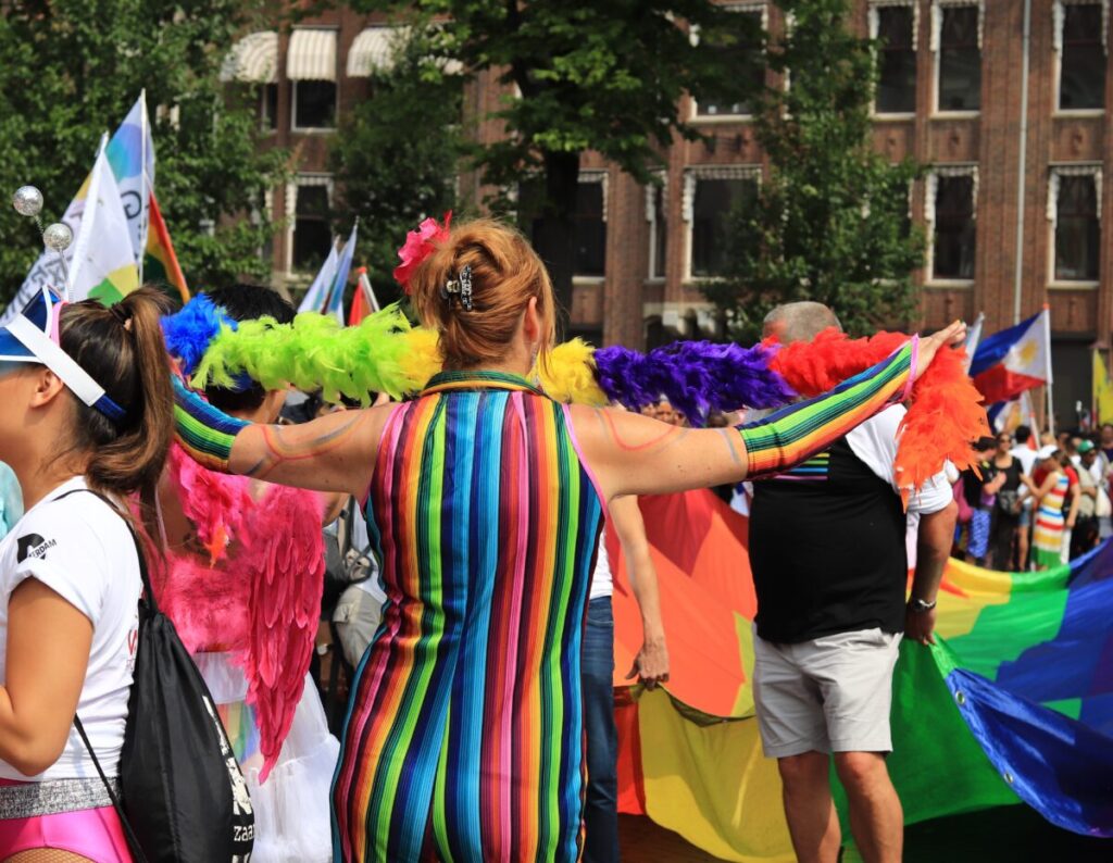 Amsterdam Pride 2026: Your Guide to the Canal Parade & Saturday Party Day 4 Woman wearing a rainbow suit and feather boa, enthusiastically celebrating at the Amsterdam Pride Parade.