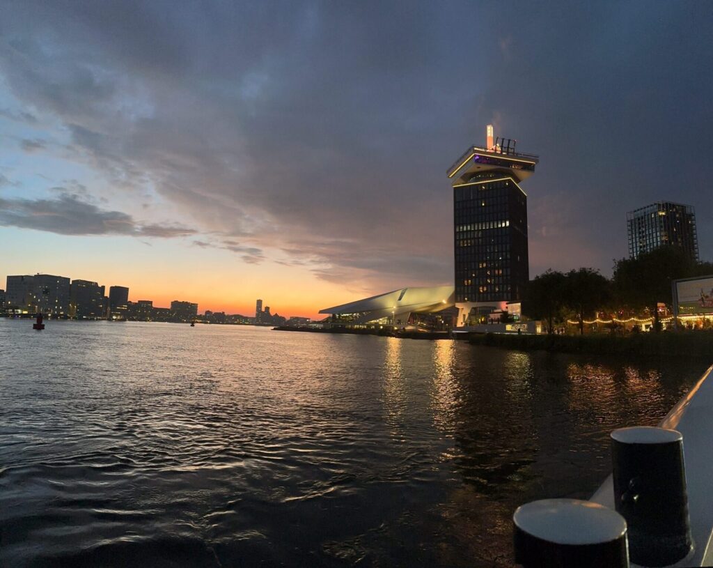 Dusk over Amsterdam canal with modern buildings and sunset reflections on water.