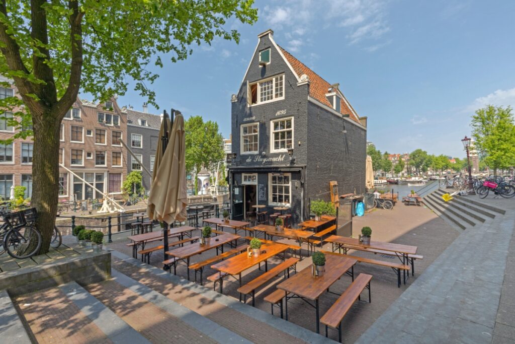 7 Captivating Leaning Houses of Amsterdam: Guide to Quirky Architectural Gems 3 Sunny spring day at Cafe De Sluyswacht, featuring outdoor tables in front of the historic 1695 building in Amsterdam