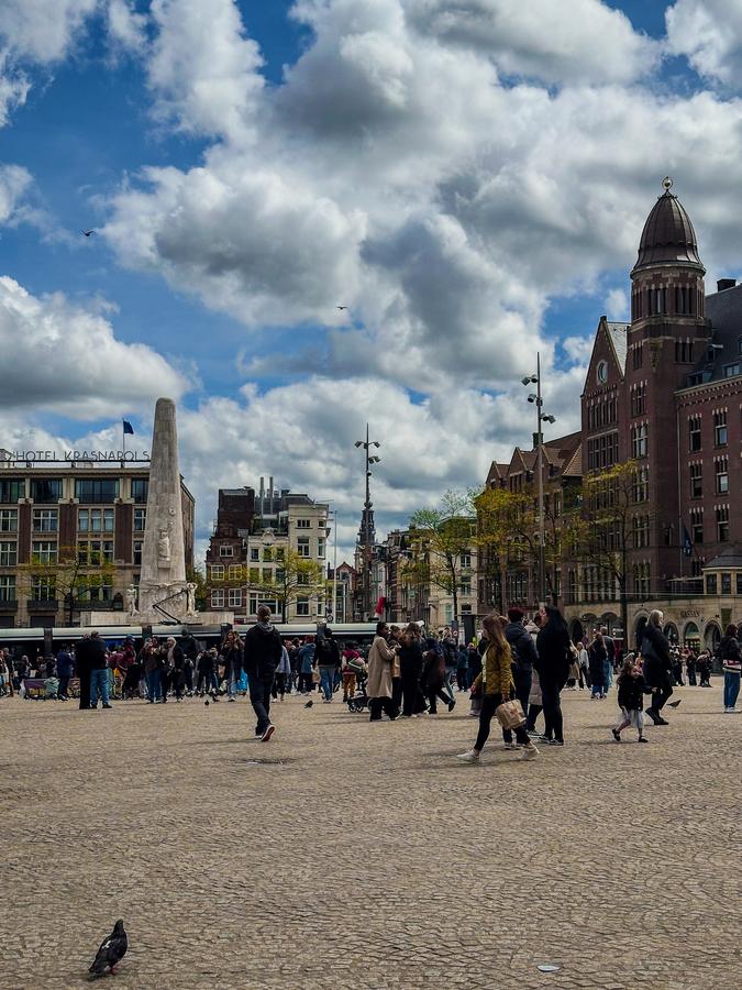 de Bijenkorf 5 Crowds crossing the cobbles of Dam Square in Amsterdam on a bright afternoon, with the National Monument obelisk at the left