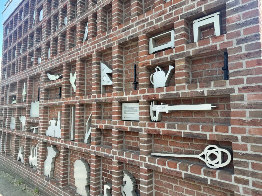 Dubbeltjespanden 7 Perspective view of the brick wall niches showing aluminum silhouettes of everyday objects and resident house numbers at Dubbeltjespanden
