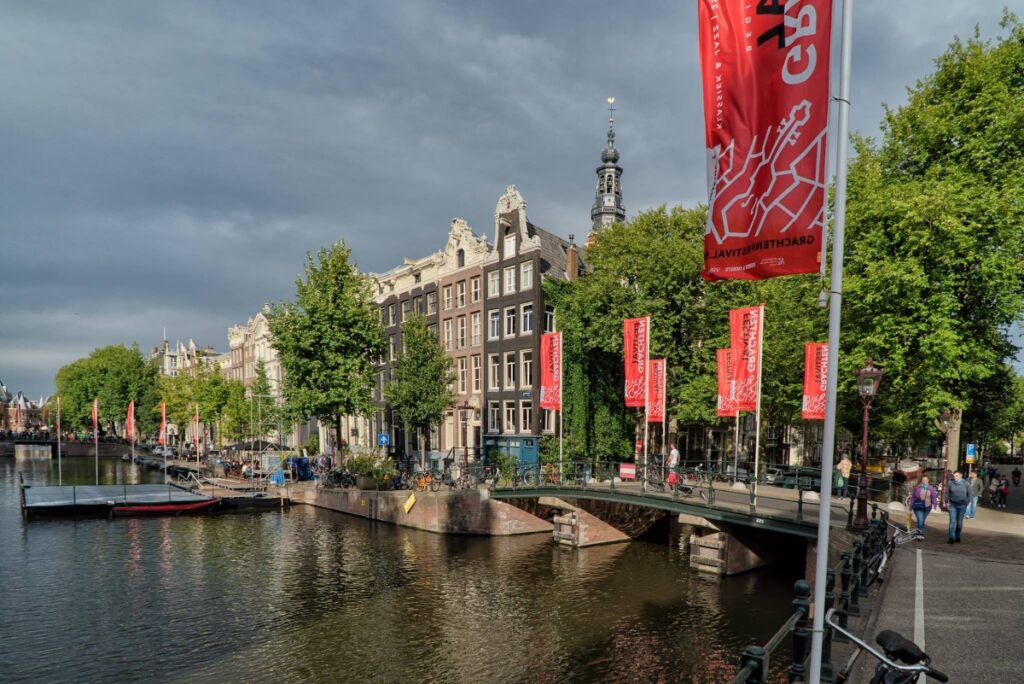 Red Grachtenfestival flags lining an Amsterdam canal bridge during the festival
