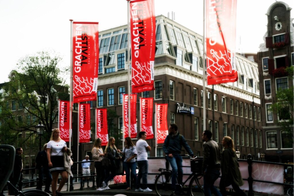 Festival-goers carrying red Grachtenfestival flags through an Amsterdam street