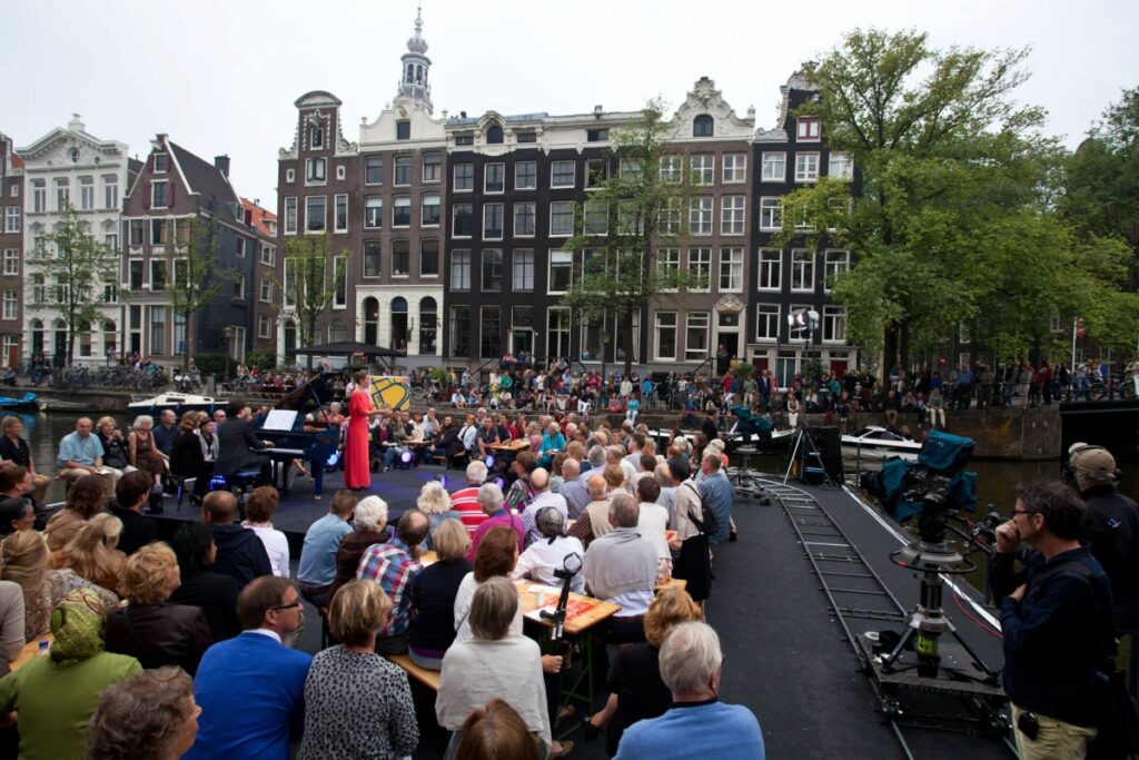 Audience on building steps watching a free canal-side Grachtenfestival concert in Amsterdam