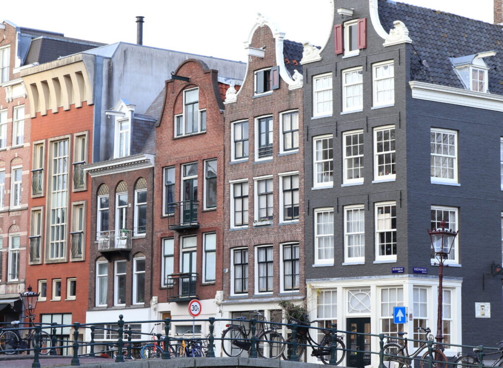 How to Find Hidden Hofjes in the Jordaan: Secret Courtyards & Local Tips 19 Courtyard in the Jordaan District, featuring a bike, plants, and views of Amsterdam Canal House facades and a bridge.