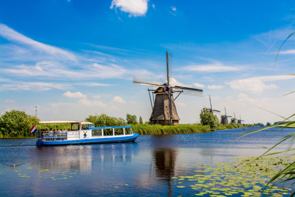 Kinderdijk vs Zaanse Schans Windmills: Which Dutch Icon Wins? 4 Canal tour boat gliding past a traditional windmill in the scenic Kinderdijk UNESCO World Heritage Site, Netherlands.