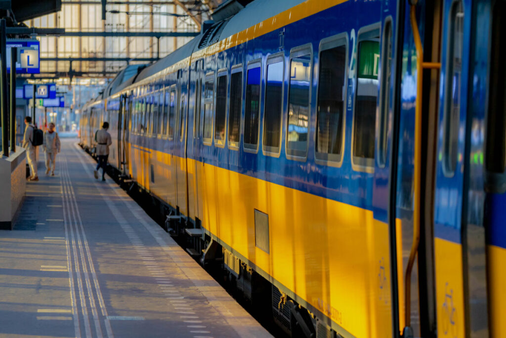 Amsterdam Airport Train vs Taxi: Which Is Better in 2026? 9 Passengers boarding a yellow and blue NS train