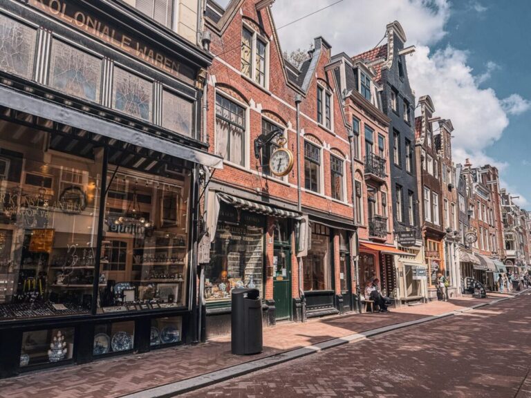 Sunlit Amsterdam street with historic architecture, shopfronts, and picturesque charm.