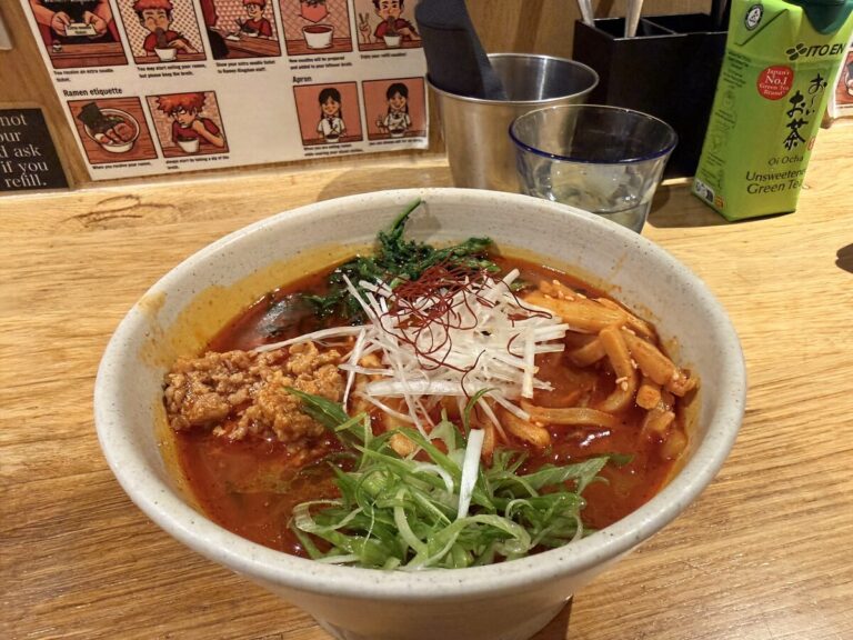 Steaming bowl of spicy ramen served at the wooden counter alongside green tea
