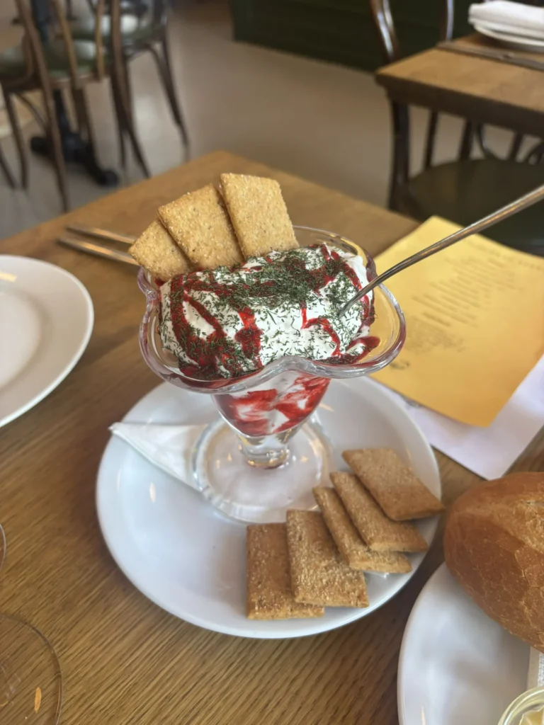 A clear glass goblet filled with panna cotta, topped with berry compote and fresh herbs, next to crackers at Restaurant Calisto.