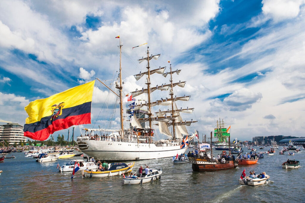 SAIL Amsterdam: 2025 Lookback and When the Next Edition Sails In (2030) 2 Big ship with a flag, featured at the SAIL Amsterdam event, alongside various other vessels in the water.