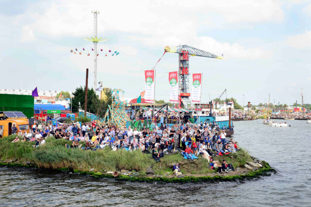 SAIL Amsterdam: 2025 Lookback and When the Next Edition Sails In (2030) 8 Group of people enjoying SAIL Amsterdam, gathered on a small island surrounded by water.