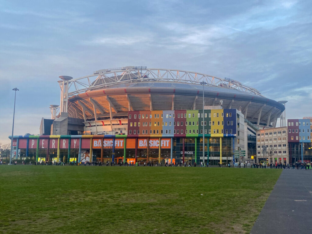 Johan Cruyff Arena 5 Modern Johan Cruyff Arena stadium with colorful commercial building in foreground and green public park area.