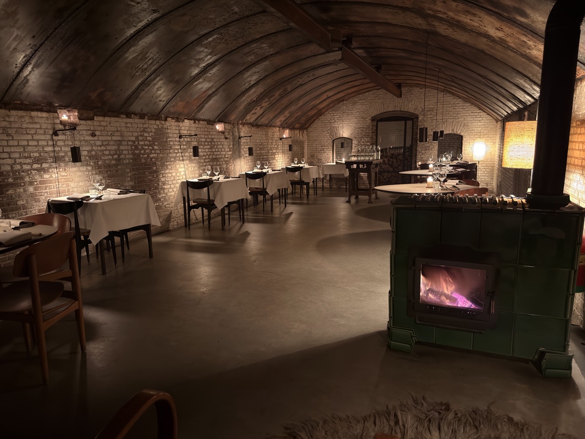 Vuurtoreneiland 9 Underground vaulted brick bunker dining room set with white tablecloths, candles, and a wood-burning stove
