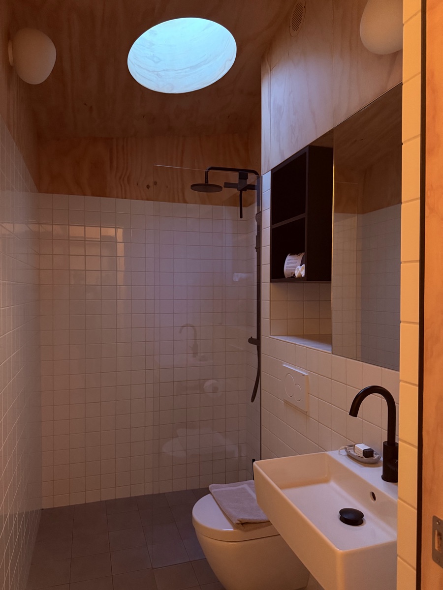 Vuurtoreneiland 21 White-tiled walk-in rain shower with circular skylight and matte black fixtures inside island cabin