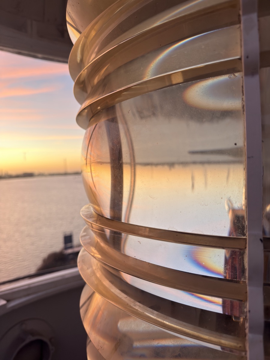 Vuurtoreneiland 15 Curved glass rings of the historic lighthouse Fresnel lens reflecting sunset light over the water