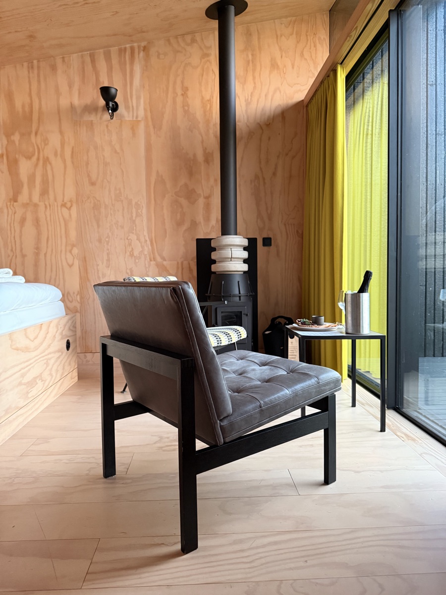 Vuurtoreneiland 19 Minimalist plywood interior of an overnight cabin on Vuurtoreneiland with leather chair and cast-iron stove