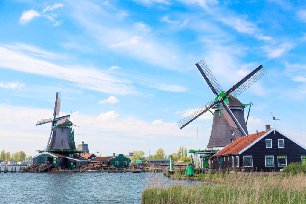 Kinderdijk vs Zaanse Schans Windmills: Which Dutch Icon Wins? 15 Scenic view of classic Dutch windmills with a blue, cloudy sky in Zaanse Schans, a famous village in the Netherlands.