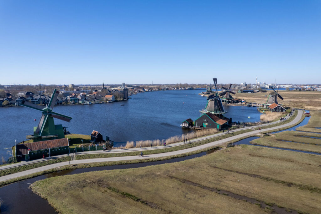 Kinderdijk vs Zaanse Schans Windmills: Which Dutch Icon Wins? 12 Traditional Dutch windmills at Zaanse Schans, surrounded by green fields and a clear blue sky.